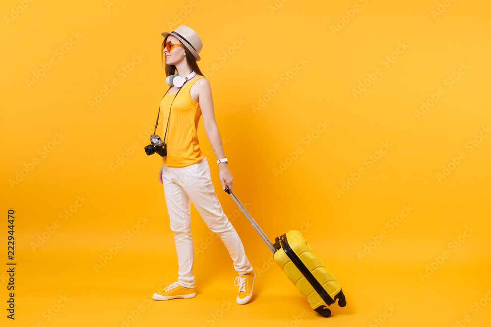 Traveler tourist woman in summer casual clothes, hat with headphones on neck isolated on yellow orange background. Passenger traveling abroad to travel on weekends getaway. Air flight journey concept. Traveler tourist woman in summer casual clothes, hat with headphones on neck isolated on yellow orange background. Passenger traveling abroad to travel on weekends getaway. Air flight journey concept.
