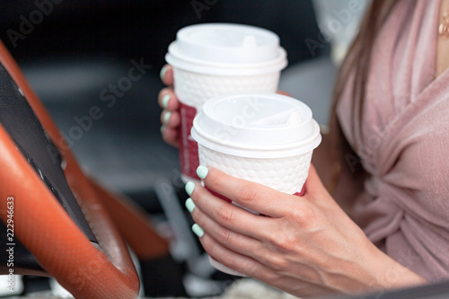 Closeup shot of hands of female driver who holds two paper cups with tea or coffee