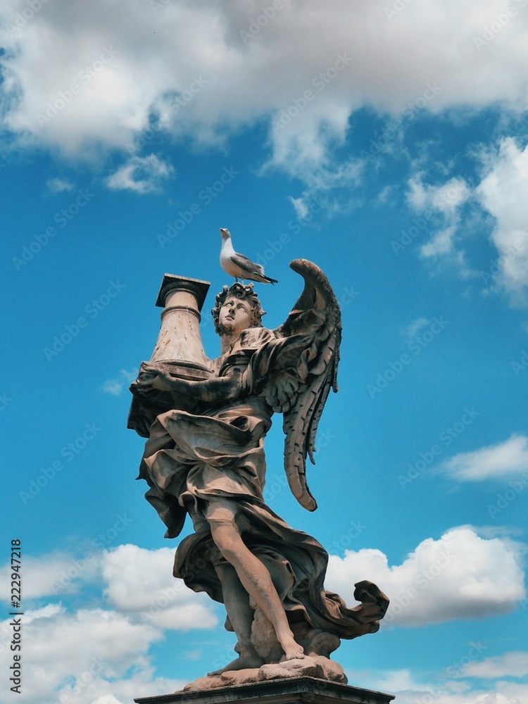 Fototapeta premium Roman sculpture on a blue sky background, located on the bridge over the Tiber river in Rome. On the head of the statue sit gulls, cormorants