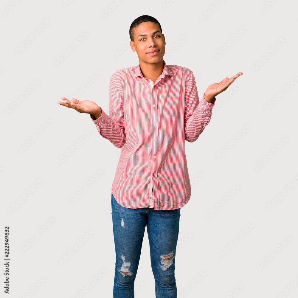 Young african american man having doubts and with confuse face expression while raising hands and shoulders Uncertain concept on grey background Young african american man having doubts and with confuse face expression while raising hands and shoulders Uncertain concept on grey background