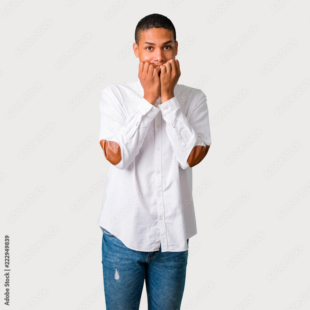 Young african american man is a little bit nervous and scared putting hands to mouth on grey background Young african american man is a little bit nervous and scared putting hands to mouth on grey background