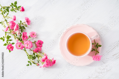 Cup of tea and branch of small pink roses on rustic table. Flat lay