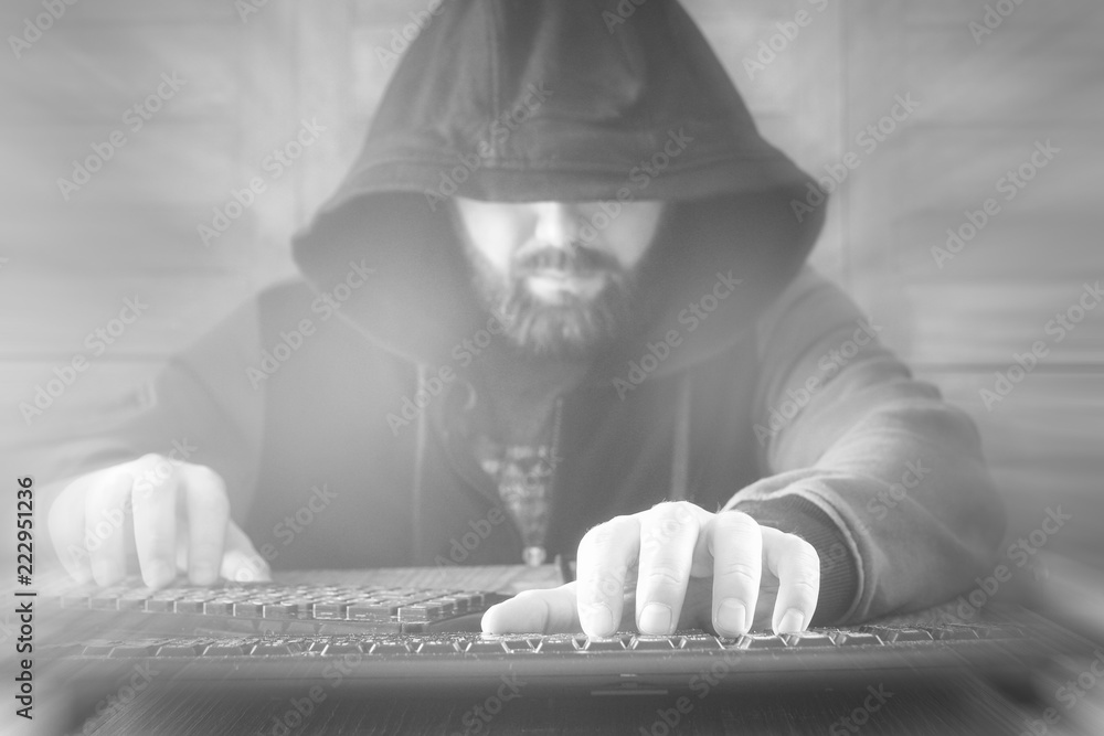 The hacker in the hood sits and works behind the computer