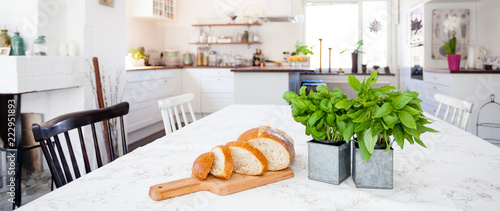 benner with fresh basil and slices of bread on the table and kitchen interior unfocused in the background