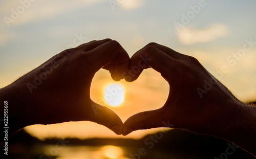 Heart gesture in front of sunset above river. Summer memories concept. Top places for romantic date. Male hands in heart shape gesture symbol of love and romance. Sunset sunlight romantic atmosphere