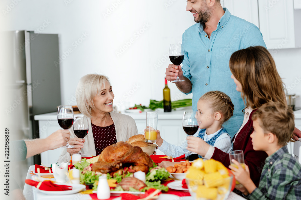 partial view of adult man with wine glass making toast at served table with turkey while his family celebrating thanksgiving partial view of adult man with wine glass making toast at served table with turkey while his family celebrating thanksgiving