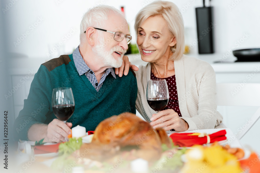 happy senior couple with wine glasses talking at served table for thanksgiving celebration