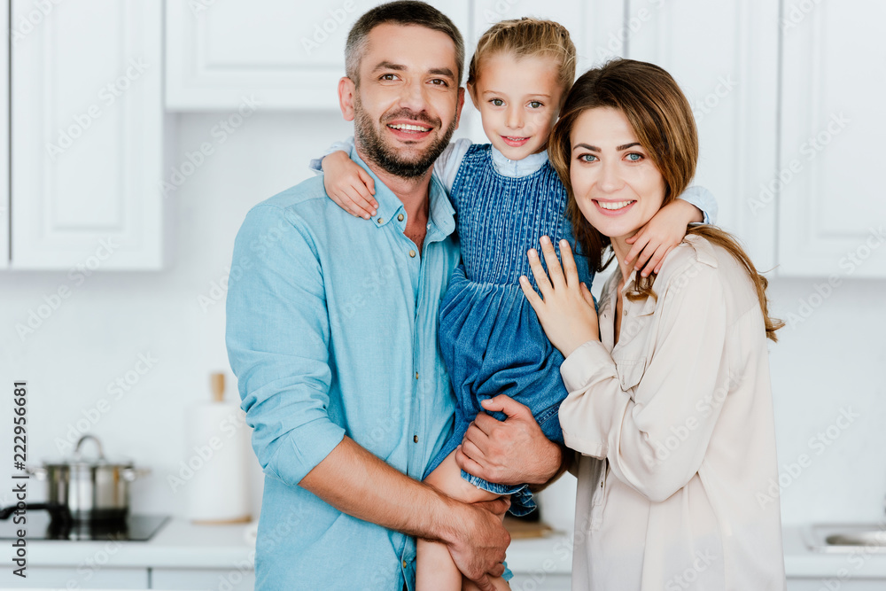 portrait of happy family holding and embracing little daughter and looking at camera at kitchen portrait of happy family holding and embracing little daughter and looking at camera at kitchen