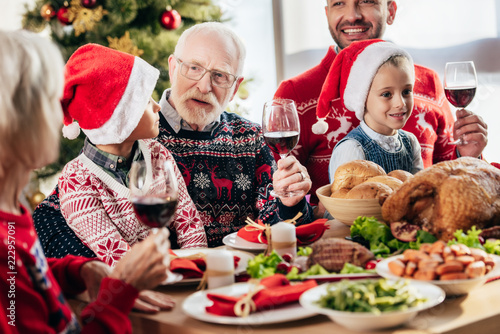 senior man with wine glass making toast during christmas celebration with family at home
