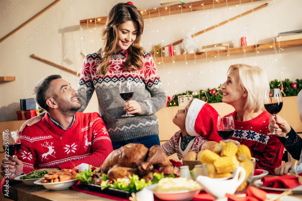 beautiful smiling woman with wine glass making toast during christmas dinner with happy family at home
