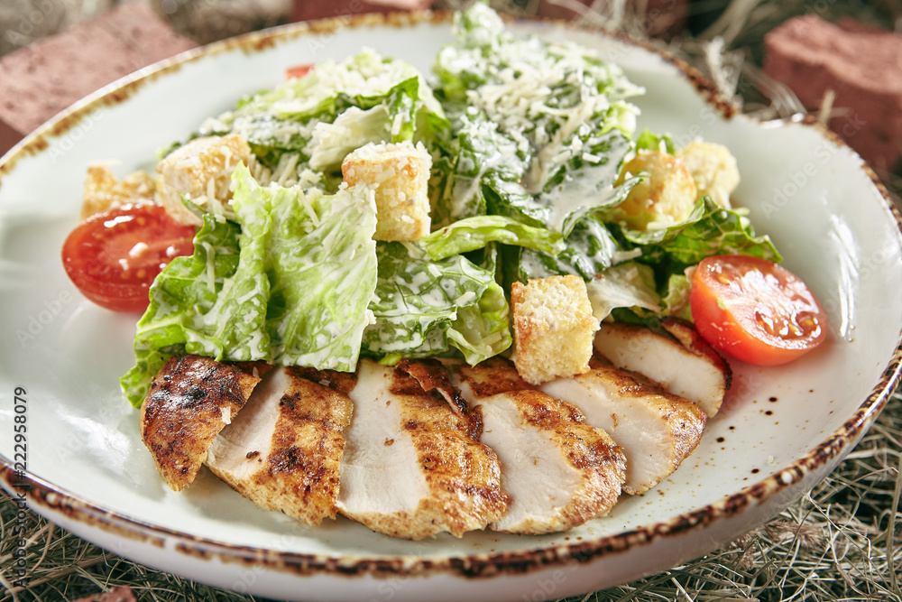 Caesar Salad with Sliced Chicken Fillet on Rustic Hay Background