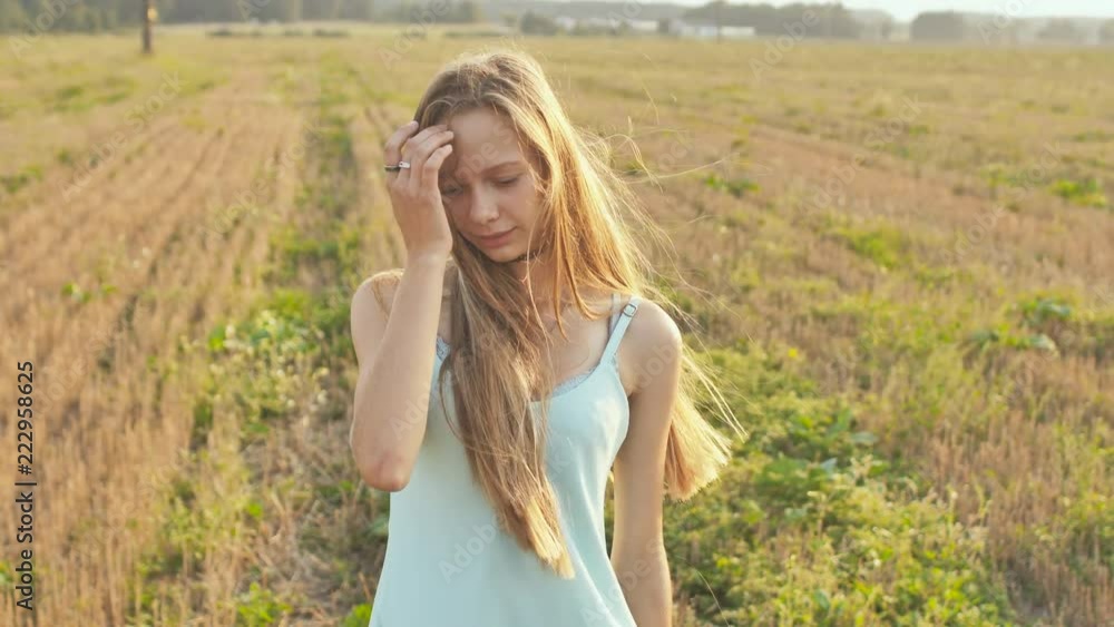 Portrait of a 16 year old girl standing in the field at dusk with long hair and a blue dress.