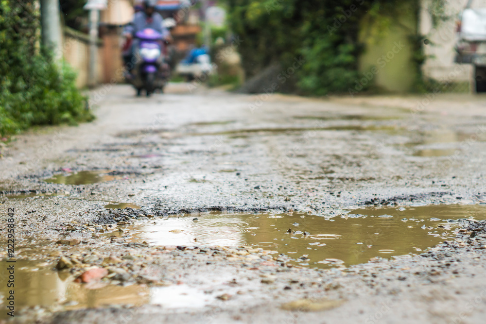 Fototapeta premium Rain falls in mud puddles in rough road, motorcycle blurred in background
