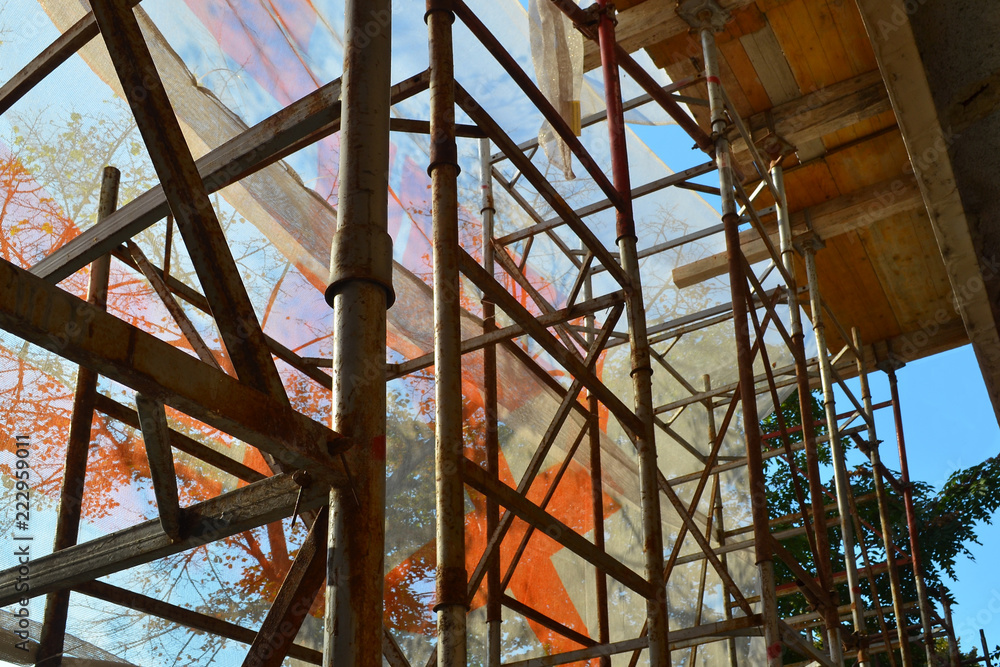 Scaffolding in front of the repaired building is shrouded with construction safety net, view from inside, sunny autumn day, horizontal frame