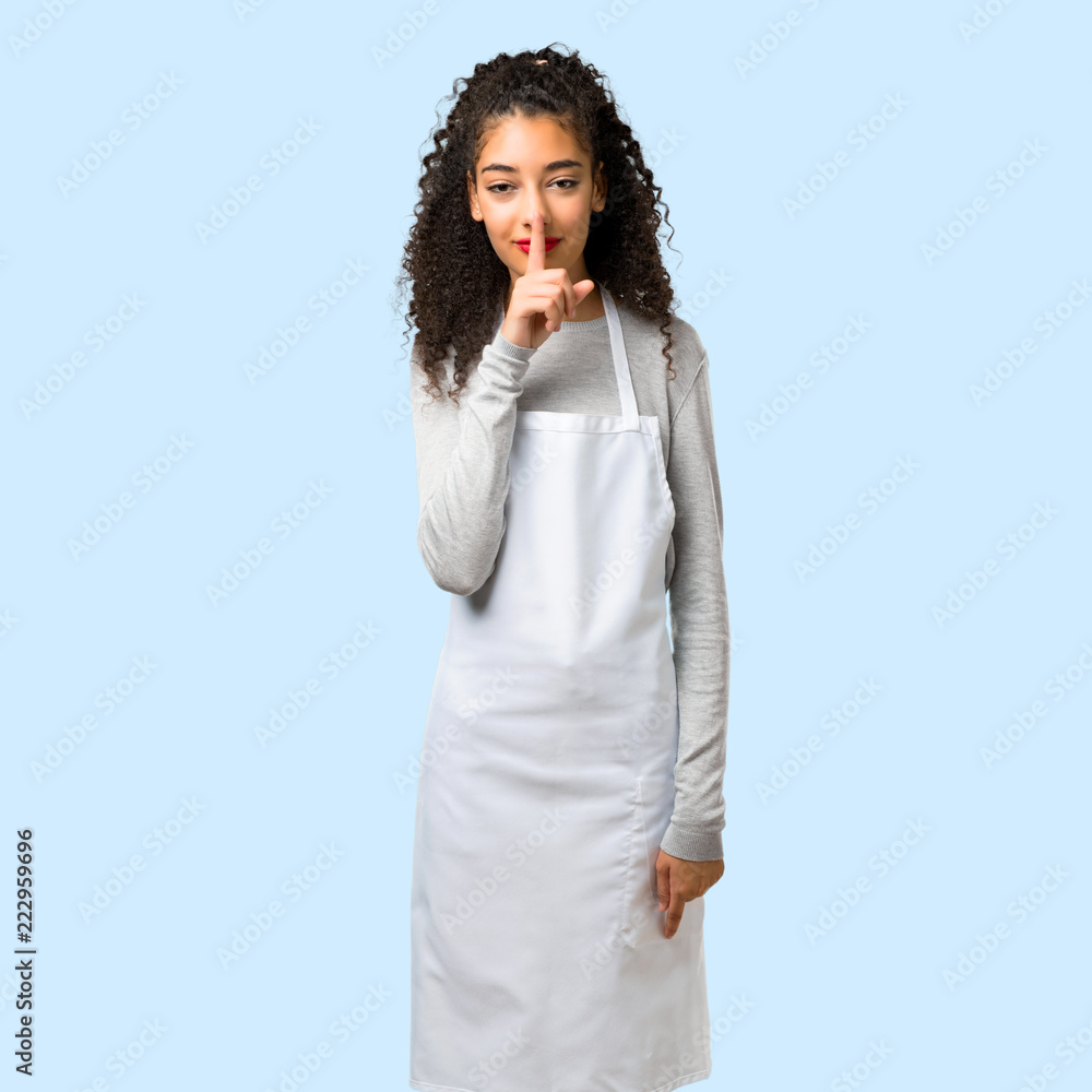 Young girl with apron showing a sign of closing mouth and silence gesture on isolated blue background