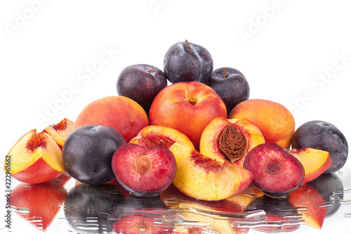 Foto A lot of bright fruits, whole and cut peaches and plums on a mirror white backgr