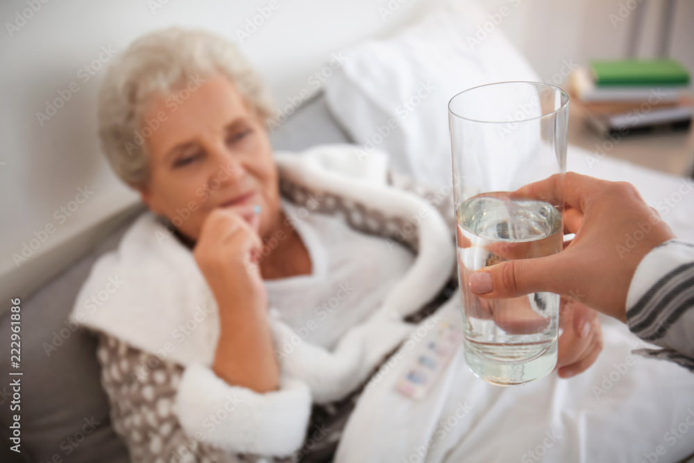 Woman giving glass of water to senior lady who is taking medicine at home Woman giving glass of water to senior lady who is taking medicine at home