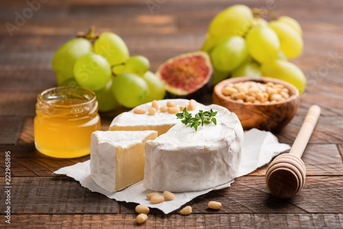 Brie or Camembert cheese with grapes, honey, figs on wooden background. Closeup view