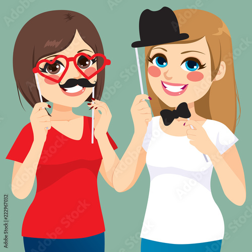 Two young teenager girls friends playing with funny pose and photo booth masks party