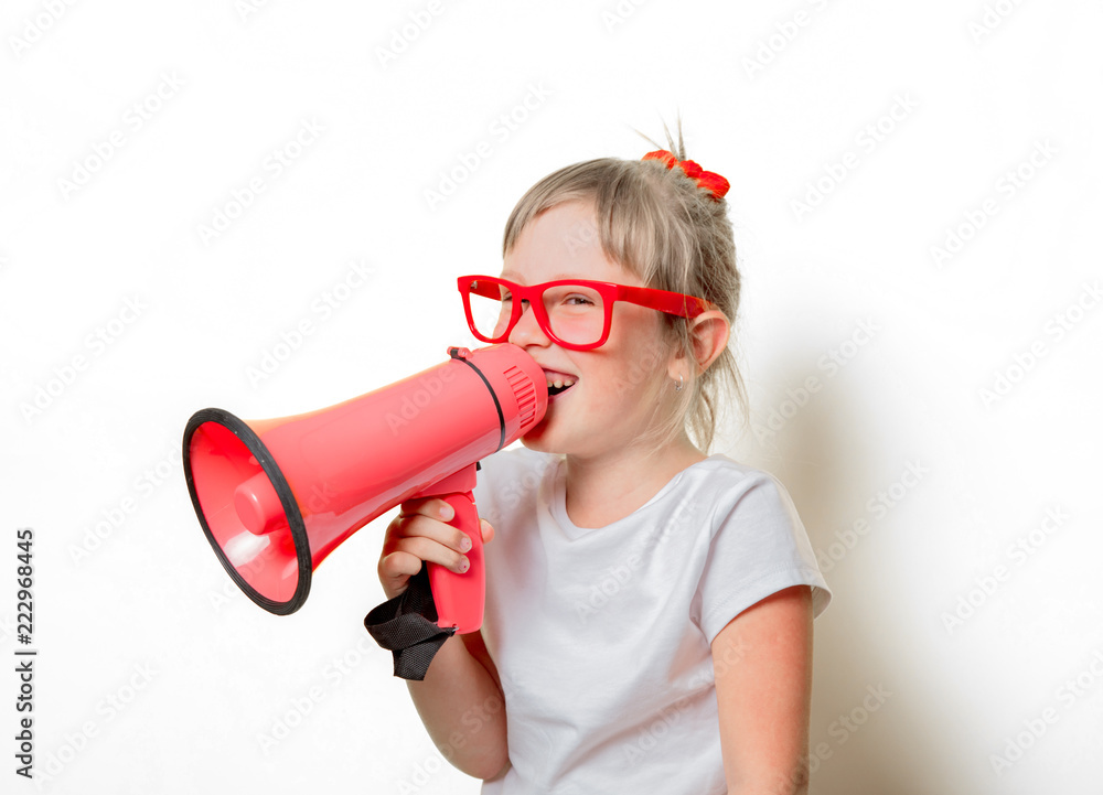 Fototapeta premium Portrait of an emotional toddler girl in glasses with megaphone on white background