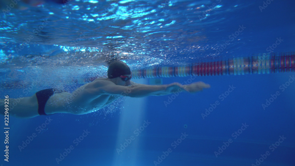Beautiful professional swimmer doing butterfly stroke in pool with rich blue water, shot from underwater