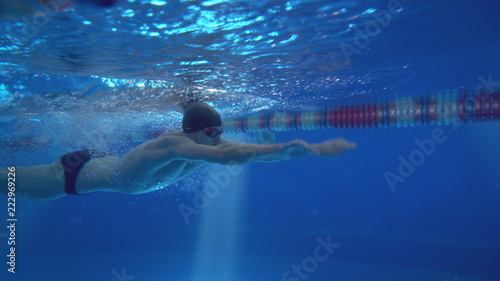Beautiful professional swimmer doing butterfly stroke in pool with rich blue water  shot from underwater