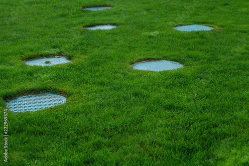 Several covers of sewer hatches on the green lawn. Green lawn with blue sewer hatches. Beautiful decor for sewer hatches. photo