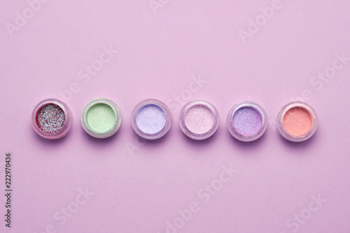Cosmetics. Makeup. Jars with crumbly bright shadows, glitter. Pink, green, lilac colors on lilac background. Closeup. Space for text or design.