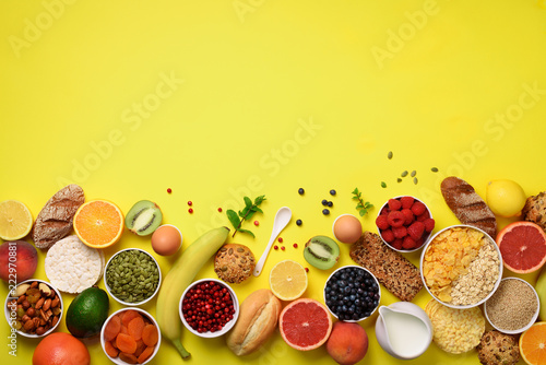 Healthy breakfast ingredients, food frame. Oat and corn flakes, eggs, nuts, fruits, berries, toast, milk, yogurt, orange, banana, peach on yellow background. Top view, copy space. Flat lay