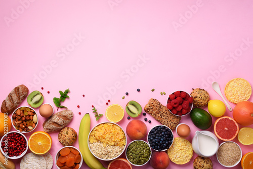 Healthy breakfast ingredients, food frame. Oat and corn flakes, eggs, nuts, fruits, berries, toast, milk, yogurt, orange, banana, peach on pink background. Top view, copy space. Flat lay
