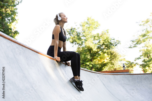 Amazing happy young sports woman sitting outdoors listening music.