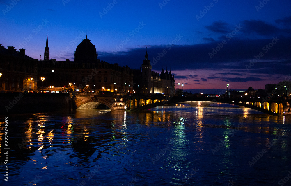 Blue hour in Paris. View of Pont au Change bridge and Conciergerie building. Colorful reflection of evening city lights in Seine river water.