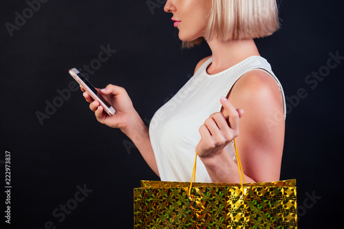 online payment for purchases Black Friday, woman using smartphone and holding shopping bag standing on the black background studio photo