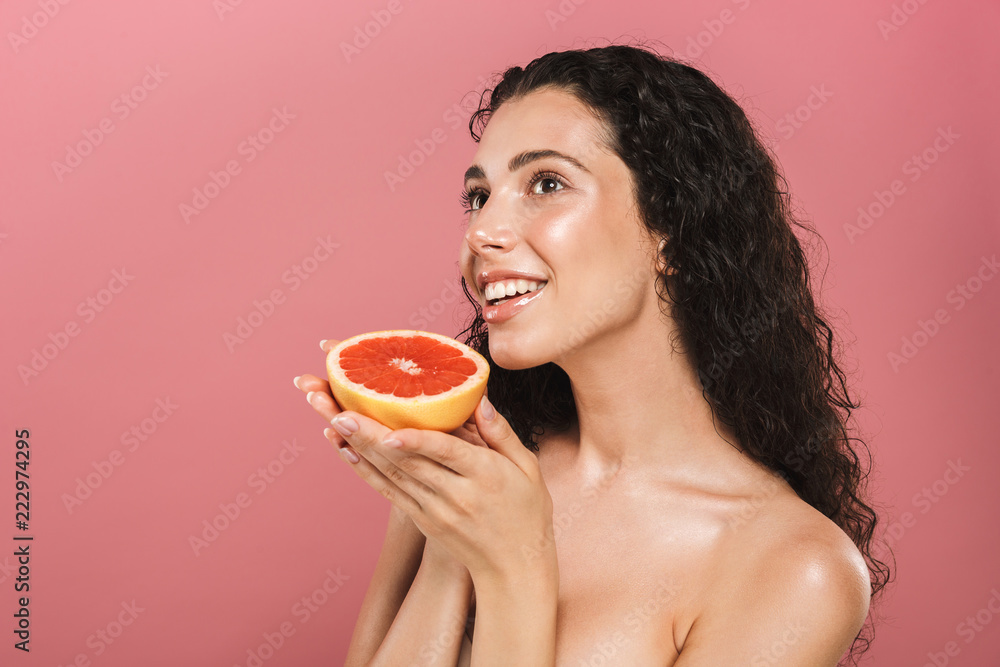 Beauty photo of caucasian woman with long hair smiling and holding piece of grapefruit, isolated over pink background Beauty photo of caucasian woman with long hair smiling and holding piece of grapefruit, isolated over pink background