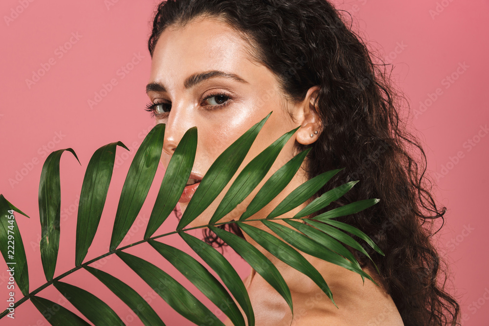 Portrait of half naked beautiful woman with long hair holding green leaf, isolated over pink background - obrazy, fototapety, plakaty 