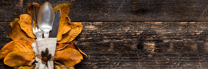 Thanksgiving Meal Setting Banner. Seasonal table setting. Thanksgiving autumn place setting with cutlery and arrangement of colorful fall leaves.
