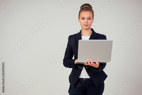 Business woman in a stylish black a jacket suit with a laptop in the studio on a white background © yurakrasil