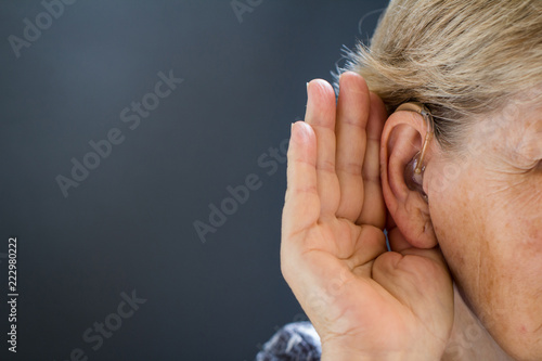 Elderly woman with hearing loss on grey background. Age related health problem.