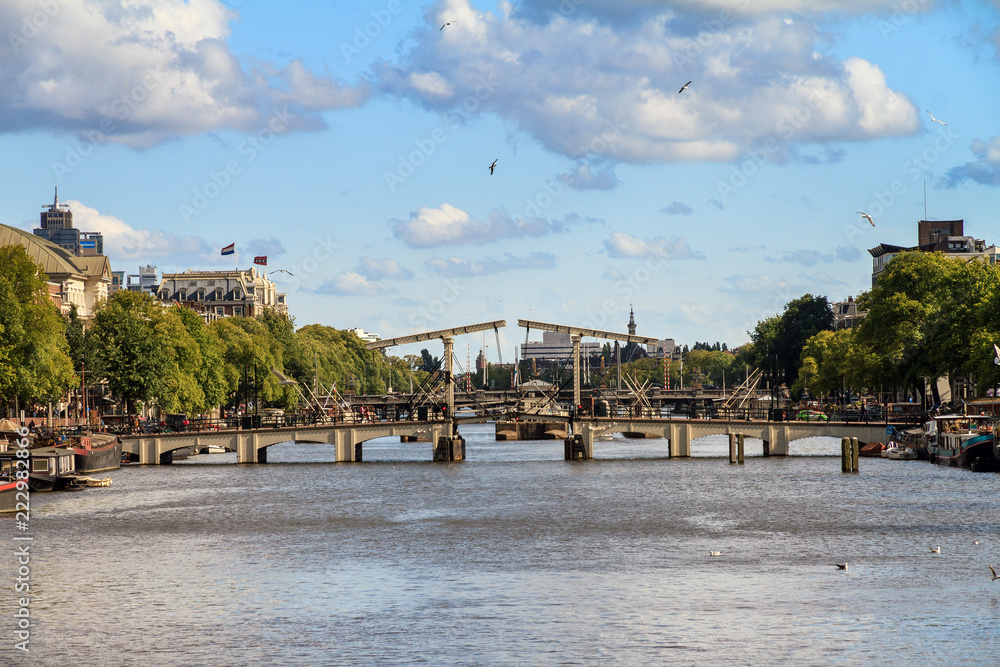 Obraz premium Piękny widok na chudy most (magere brug) nad rzeką Amstel w Amsterdamie w Holandii w słoneczny letni dzień z chmurami i ptakami