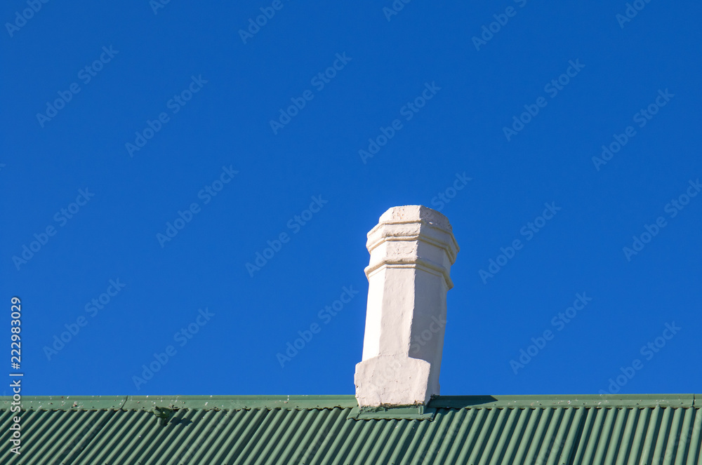 A brilliant white chimney on a green corrugated zinc roof against a clear blue sky image with copy space in landscape format