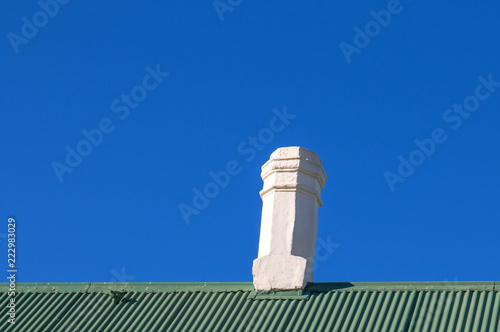 A brilliant white chimney on a green corrugated zinc roof against a clear blue sky image with copy space in landscape format