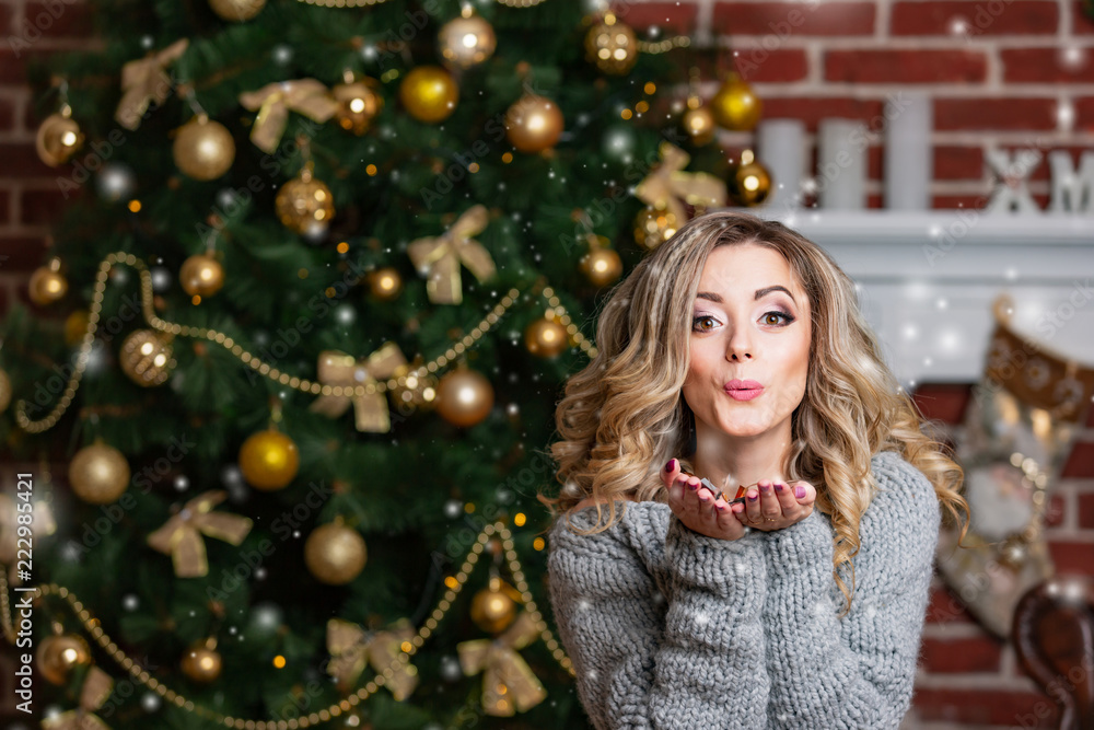 happy beautiful woman in gray dress sends an air kiss on the background of a Christmas tree with balls happy beautiful woman in gray dress sends an air kiss on the background of a Christmas tree with balls