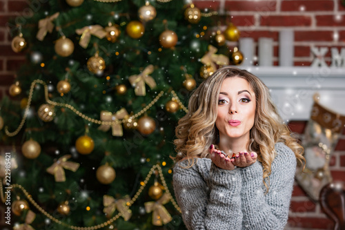 happy beautiful woman in gray dress sends an air kiss on the background of a Christmas tree with balls