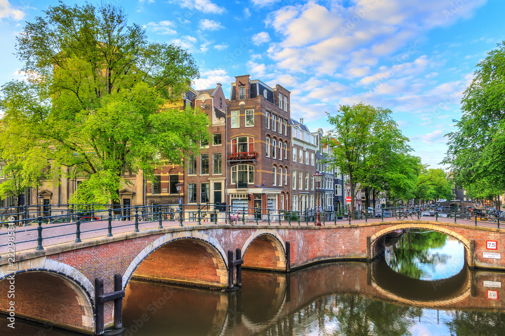 Fototapeta premium Piękny widok na kultowe kanały światowego dziedzictwa UNESCO Prinsengracht i Reguliersgracht w Amsterdamie w Holandii w słoneczny letni poranek z błękitnym niebem i refleksami