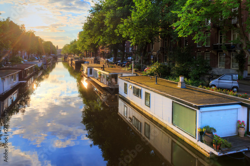 Houseboats at the UNESCO world heritage canals of Amsterdam, The Netherlands, on a sunny summer morning with a blue sky and clouds and a mirror reflection
