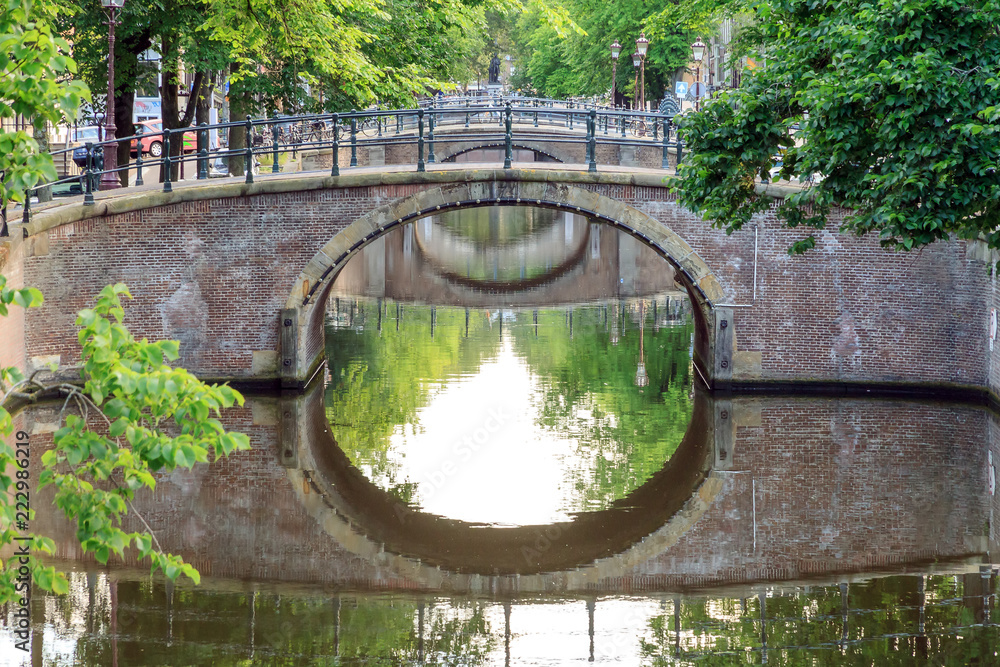 Obraz premium Piękny letni poranek widok na mosty nad słynnym kanałem Reguliersgracht światowego dziedzictwa UNESCO w Amsterdamie, Holandia, z lustrzanym odbiciem