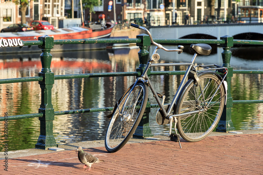 Bicycle on a bridge on the famous world heritage canals of Amsterdam, The Netherlands, on a sunny summer day with a pigeon
