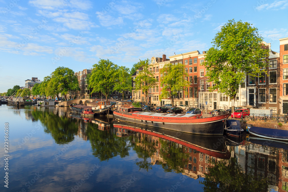 Beautiful sunrise morning view of houseboats in the river Amstel in Amsterdam, the Netherlands, on a sunny summer day with a mirror reflection