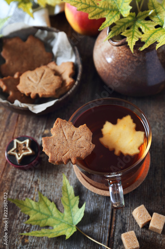 Autumn mood: cinnamon cookies in form of maple leaves, tea, red apple and yellow leaves