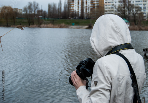 A girl in a white jacket takes pictures of nature near the lake